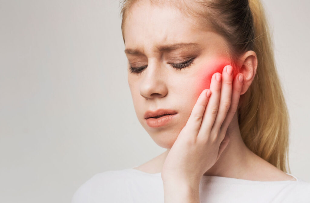 A woman is suffering from a toothache, she's touching and pressing her cheek with a gesture of pain in her face. There is a red glow on her cheek indicating where the pain is.