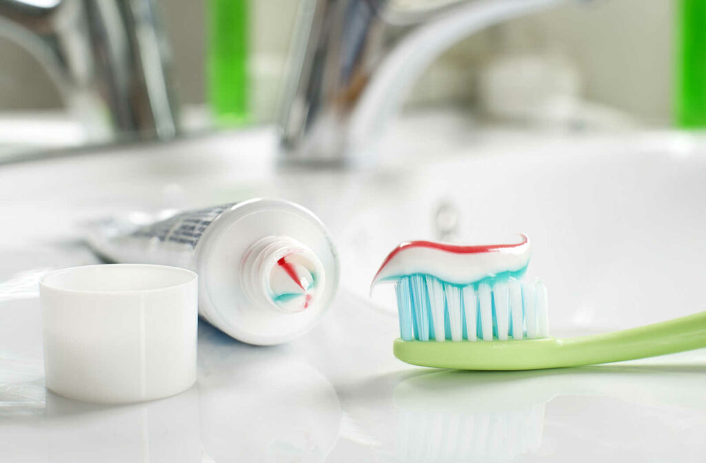 A toothbrush with toothpaste and a tube of toothpaste in the background.