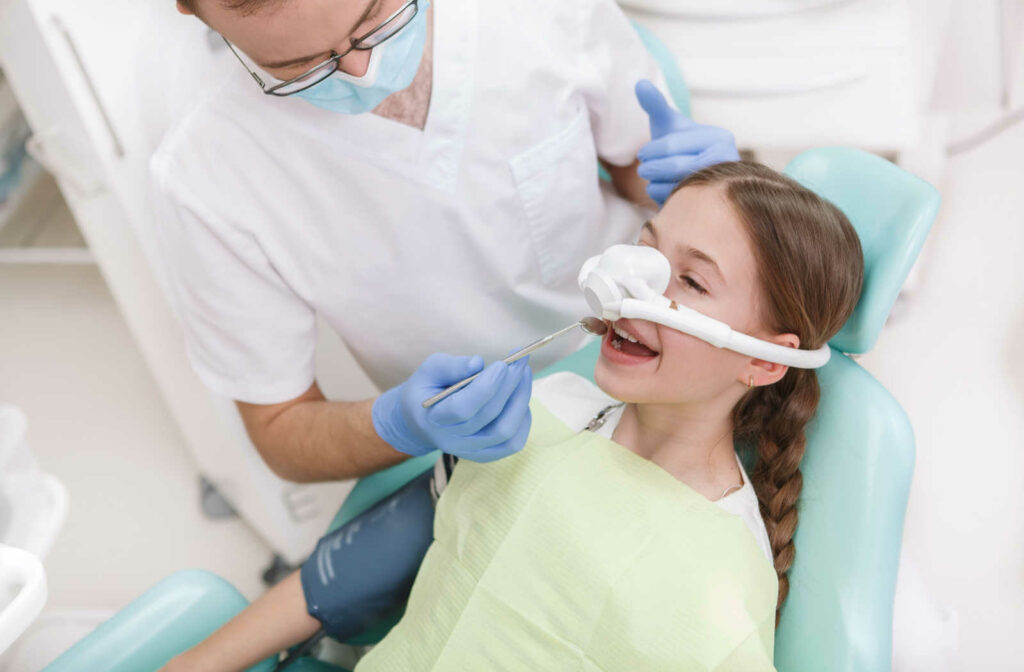 A young girl sitting on a dental chair is having her teeth treated while having an inhalation sedation mask on.