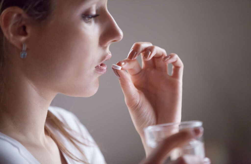 A close-up of a girl holding a glass of water and taking a sedation pill at the dental clinic.