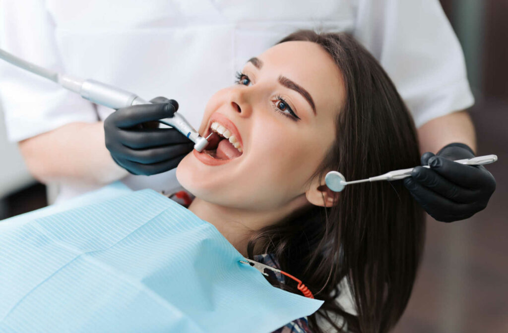 A beautiful young woman seated in a dentist chair as her dentist checks and cleans her teeth.