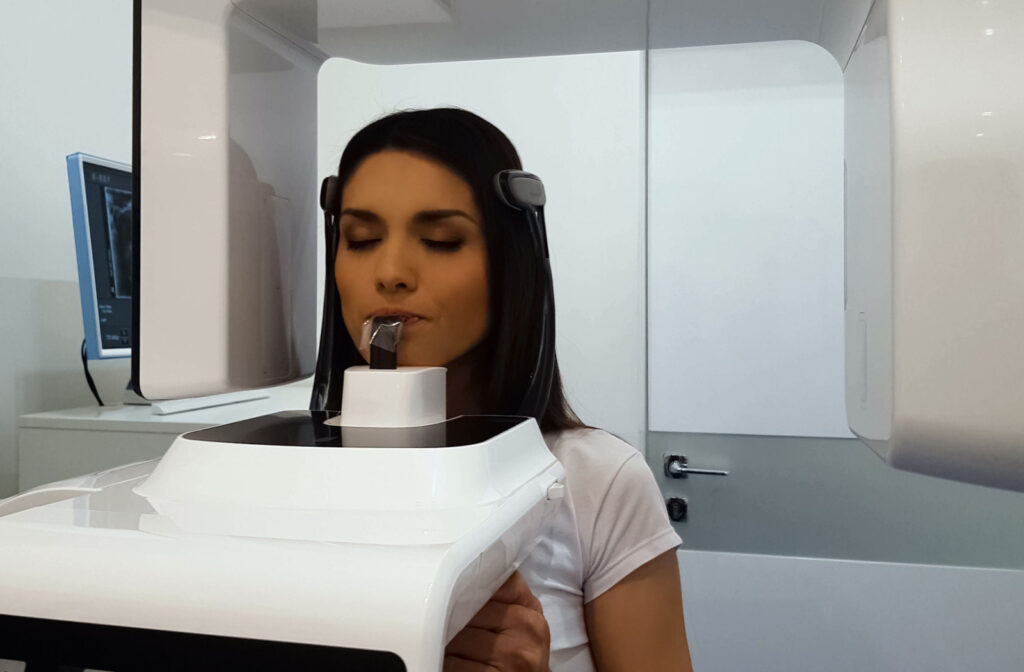 A young woman resting her chin and biting down on a specialized device during a dental X-ray exam.